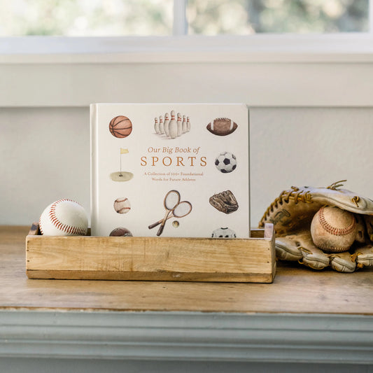 Book titled 'Our Big Book of Sports' on a wooden stand with sports-themed items.