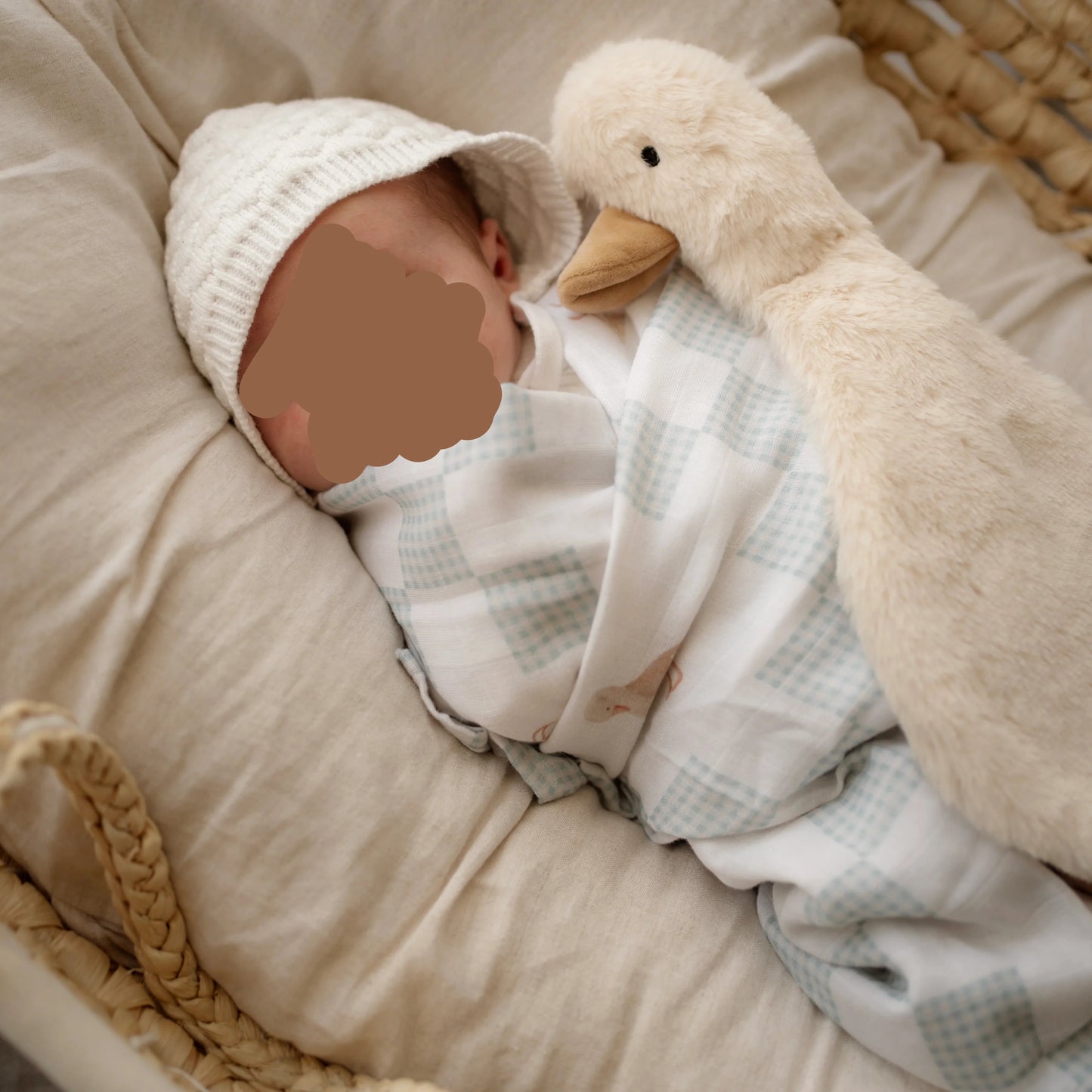 Newborn baby wrapped in neutral goose muslin swaddle with plush comforter toy