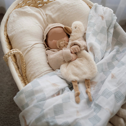 Sleeping newborn baby styled with neutral goose swaddle blanket and soft comforter toy