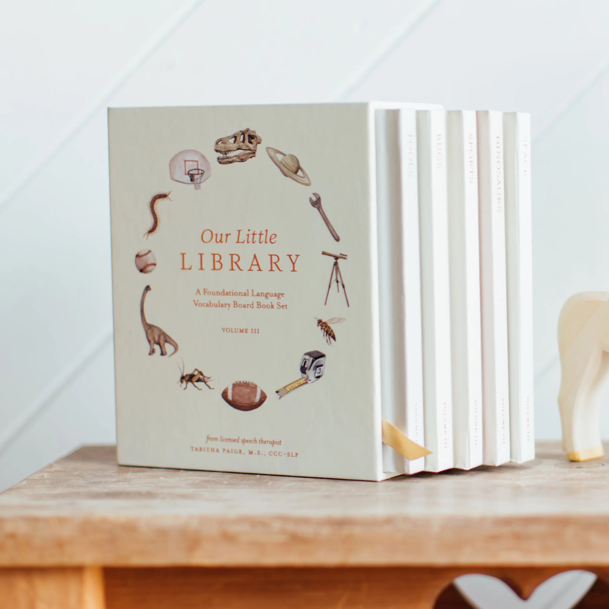 Set of children's books titled 'Our Little Library' on a wooden surface with a white geometric patterned wall in the background.