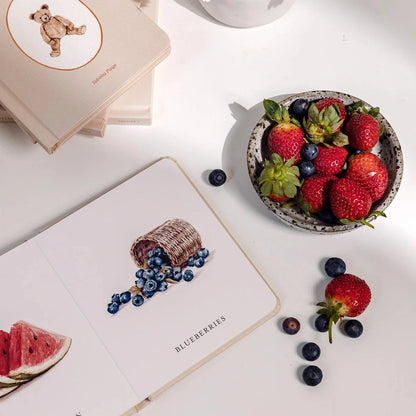 Fruits and flowers on a white surface with decorative cards.