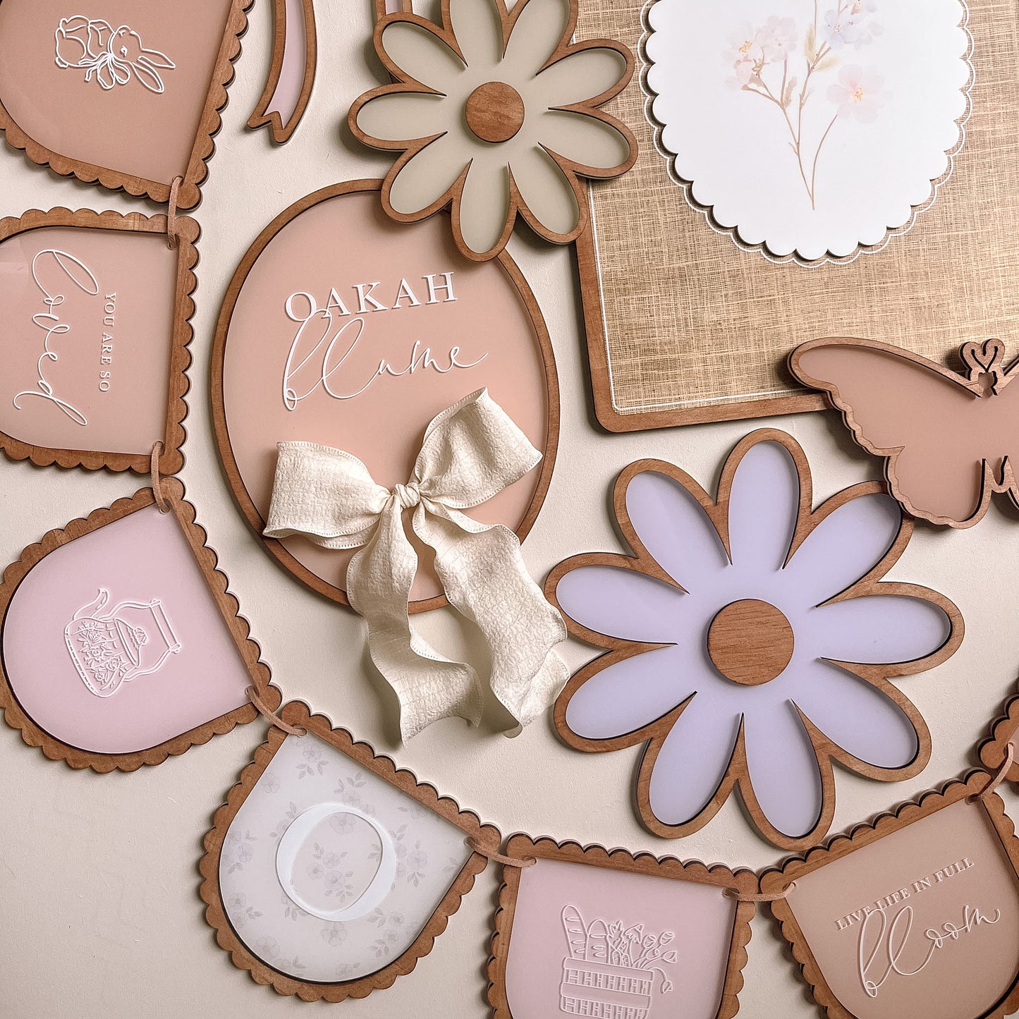 Neutral toned nursery wall decor set featuring personalised name plaque, daisy shapes, butterfly detail and custom banner
