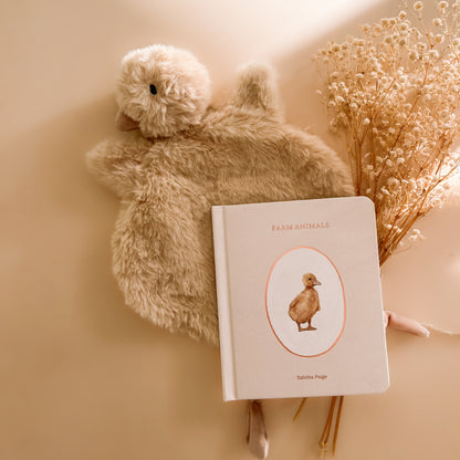 Soft duck baby comforter styled with neutral farm animal baby book and nursery décor