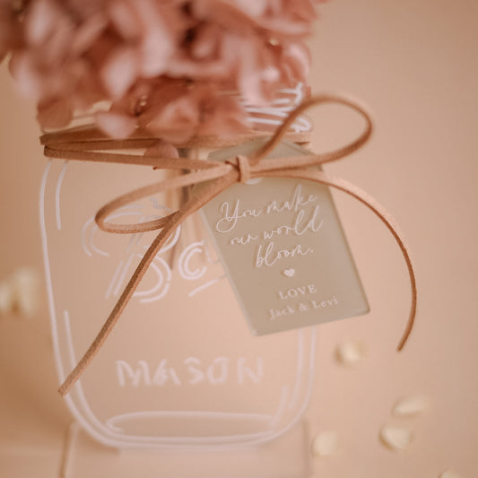 Acrylic mason jar keepsake with dried florals ribbon and personalised message tag on soft beige background
