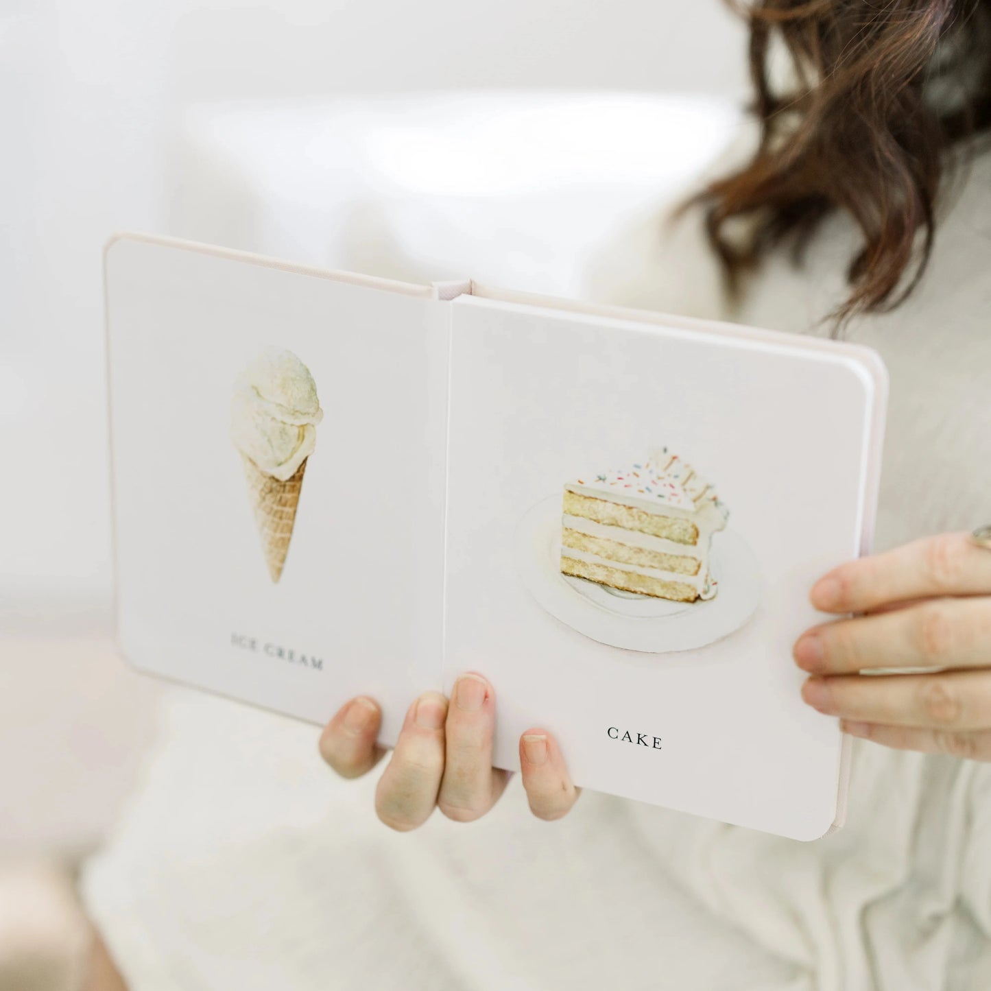Person holding a white notebook with ice cream and cake illustrations on a light background
