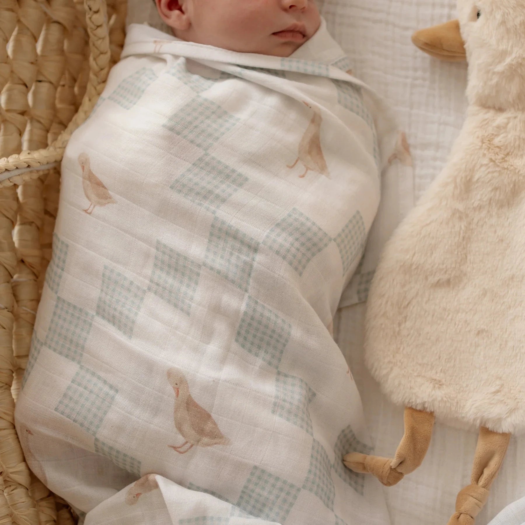 Newborn baby wrapped in neutral goose swaddle blanket with soft nursery styling