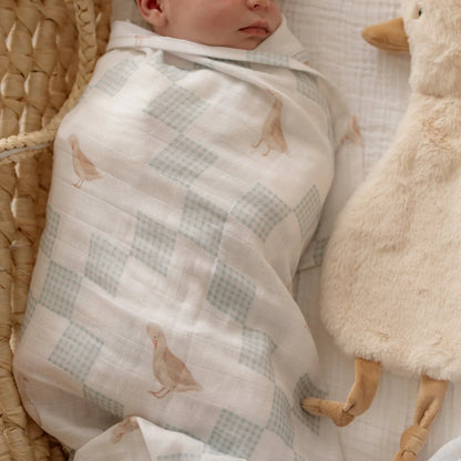 Newborn baby wrapped in neutral goose swaddle blanket with soft nursery styling