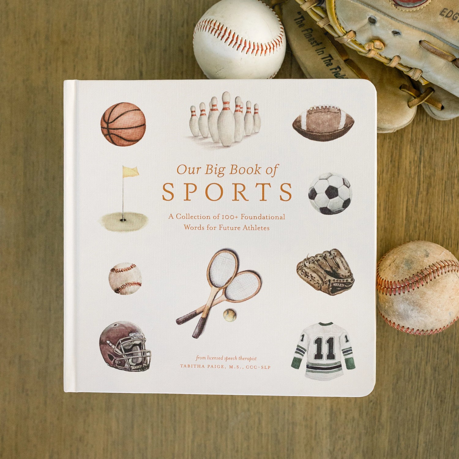 Book titled 'Our Big Book of Sports' with sports-themed illustrations on a wooden surface.