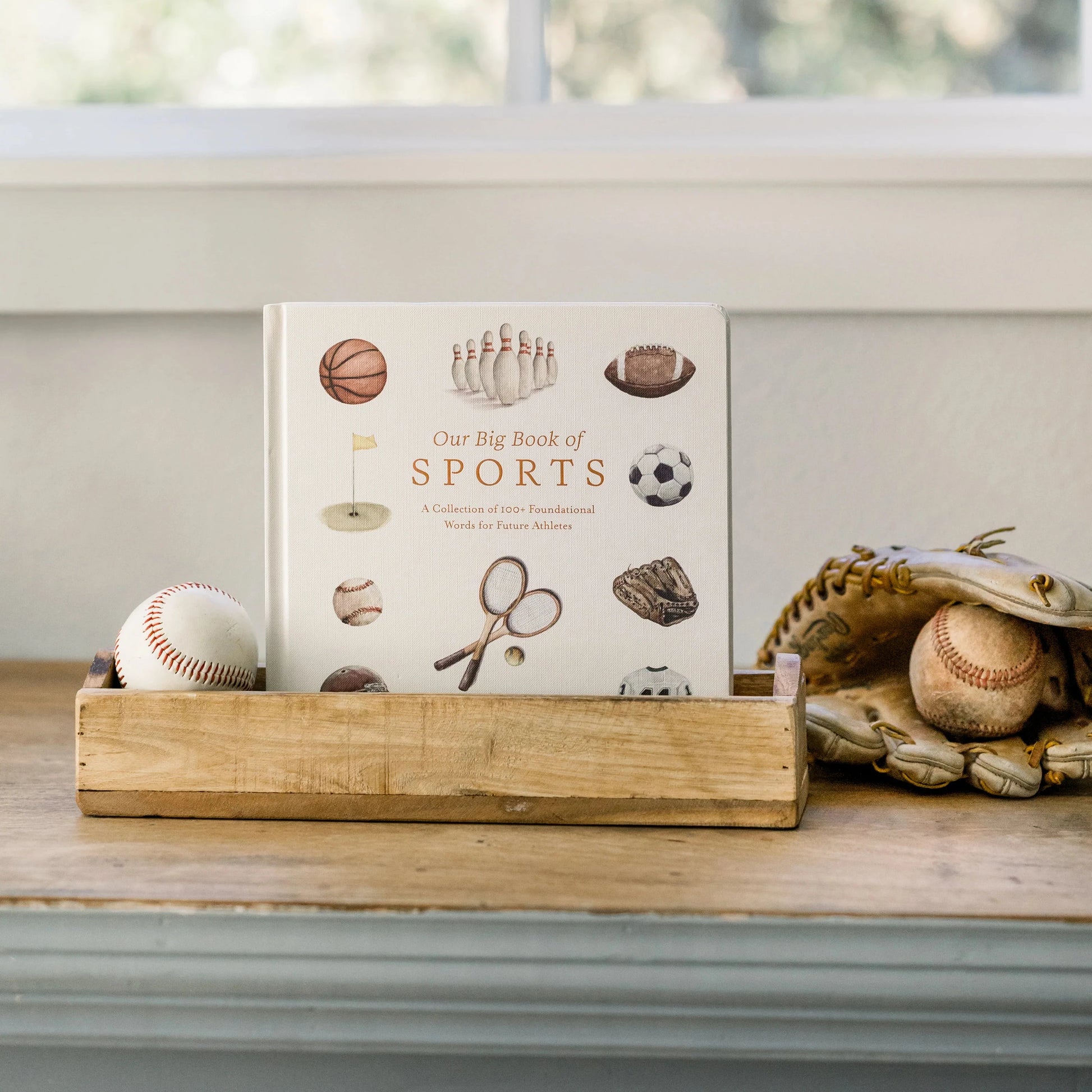 Book titled 'Our Big Book of Sports' on a wooden stand with sports-themed items.