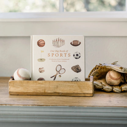 Book titled 'Our Big Book of Sports' on a wooden stand with sports-themed items.